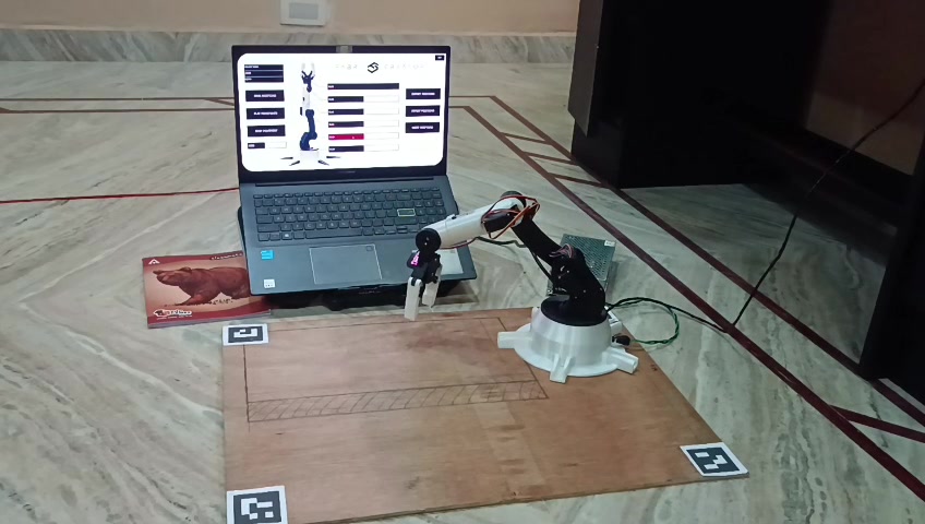 Mid-reach, with the ArUco-tagged workspace and the host control interface visible.