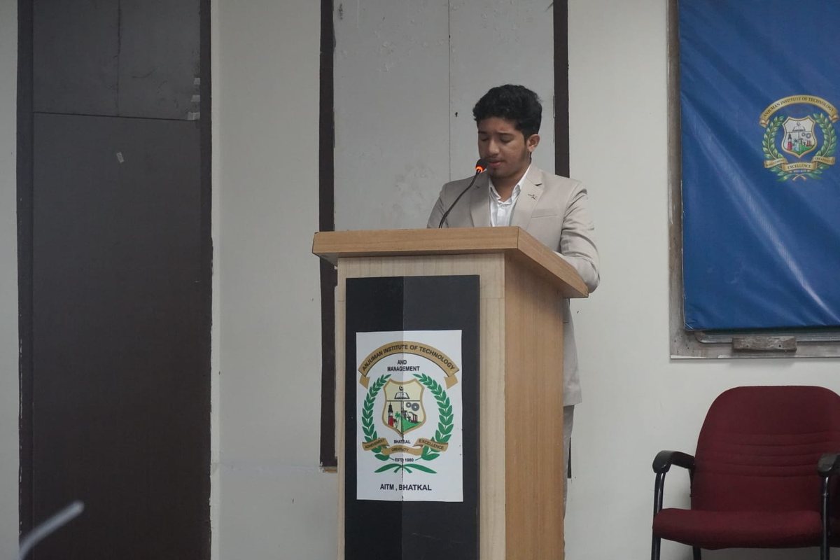Speaking at a podium with the AITM crest